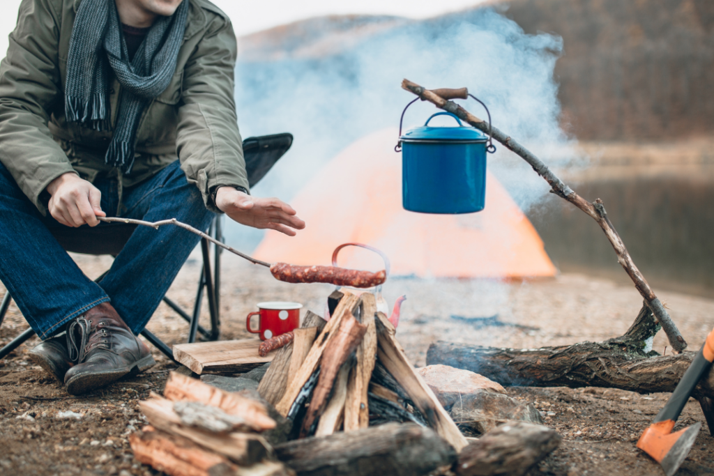 a person sitting next to a campfire with a blue pot